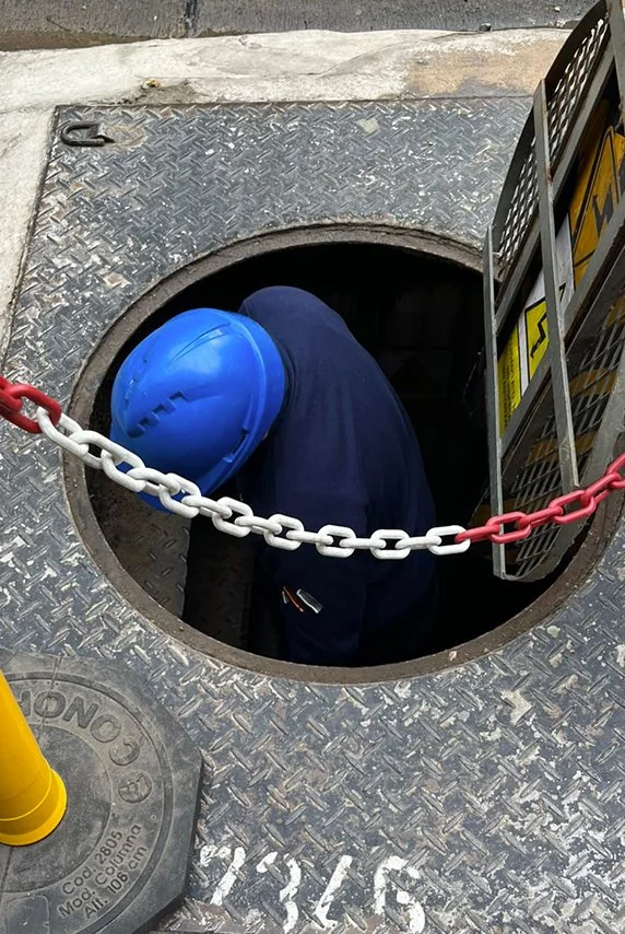 Técnico con casco ingresando a una cámara subterránea por la boca de inspección